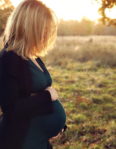 Reading maternity photographer Ania Chandra - pregnant women is looking down on her belly and sun is gazing over her hair