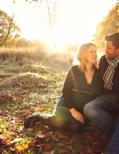 Ania Chandra maternity Photographer in Reading and beyond. Photo of pregnant mama with her husband sitting down on the tree during sunset in Richmond Park in London. They look in love and very happy looking at each other
