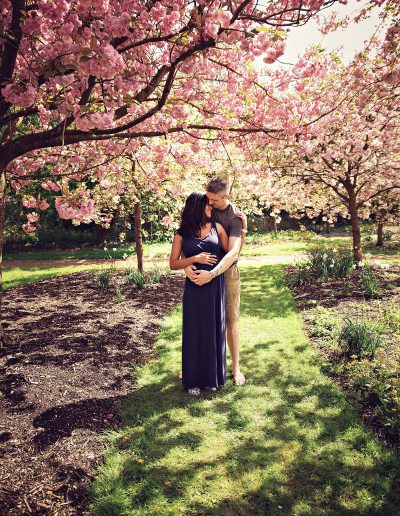 Ania Chandra Photography in Berkshire, Reading Harris Garden. Cape are standing under the blossom tree and holding each other with love. Mama is pregnant and happy