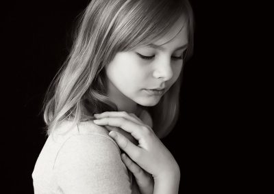 School Photography Reading Ania Chandra, Girl on the black background looking down and her hands are resting on the shoulder, artistic photo