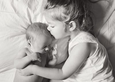 Berkshire newborn photographer, toddler is holding nd=ewborn baby and kissing him on his forhead - very cute and emotional black and white photo - on the bed