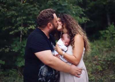newborn photographer ania chandra in Reading - parents kissing and holding thir little baby in beautiful nature