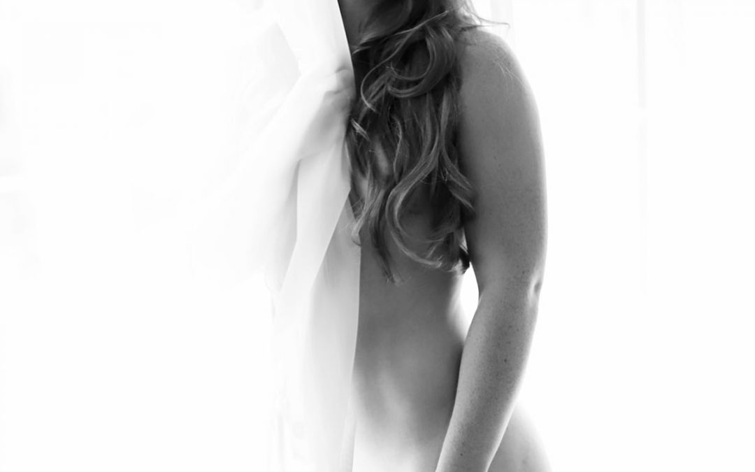 naked women is standing next to he window and her hair are covering her breast and she is covered holding white curtain. Ania chandra photographer in Reading - Boudoir image