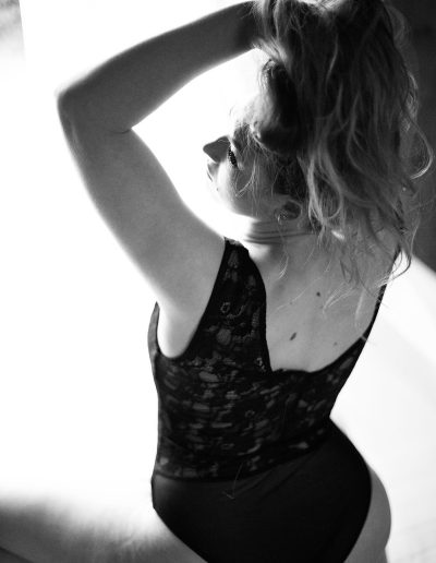 boudoir women seating on the chair in body suit lifting her hair - Black and white boudoir image done by aniachandra photography