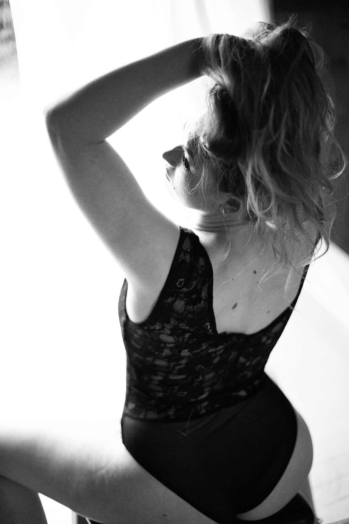 boudoir women seating on the chair in body suit lifting her hair - Black and white boudoir image done by aniachandra photography